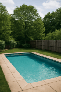 Pristine rectangular pool surrounded by a beige sandstone deck and lush greenery in a backyard in Meriden, CT.