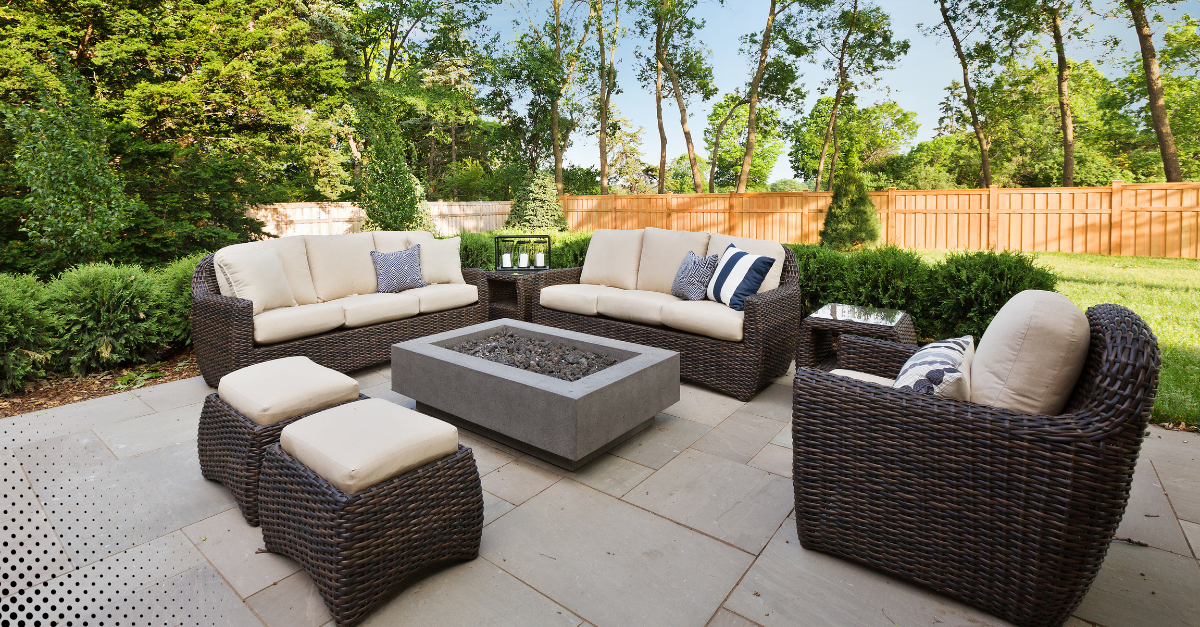 Cozy outdoor patio setup with cushioned wicker seating and a modern fire pit surrounded by greenery.
