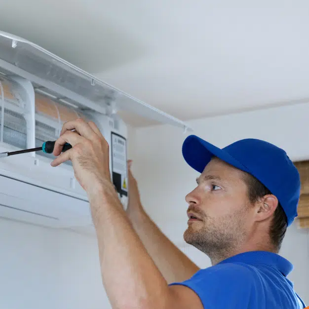 Technician servicing an outdoor HVAC unit with tools and gear on the ground.