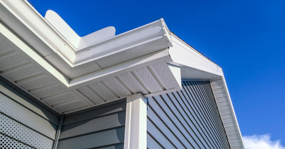 Close-up of house roof, soffit, and gutter under clear blue sky.