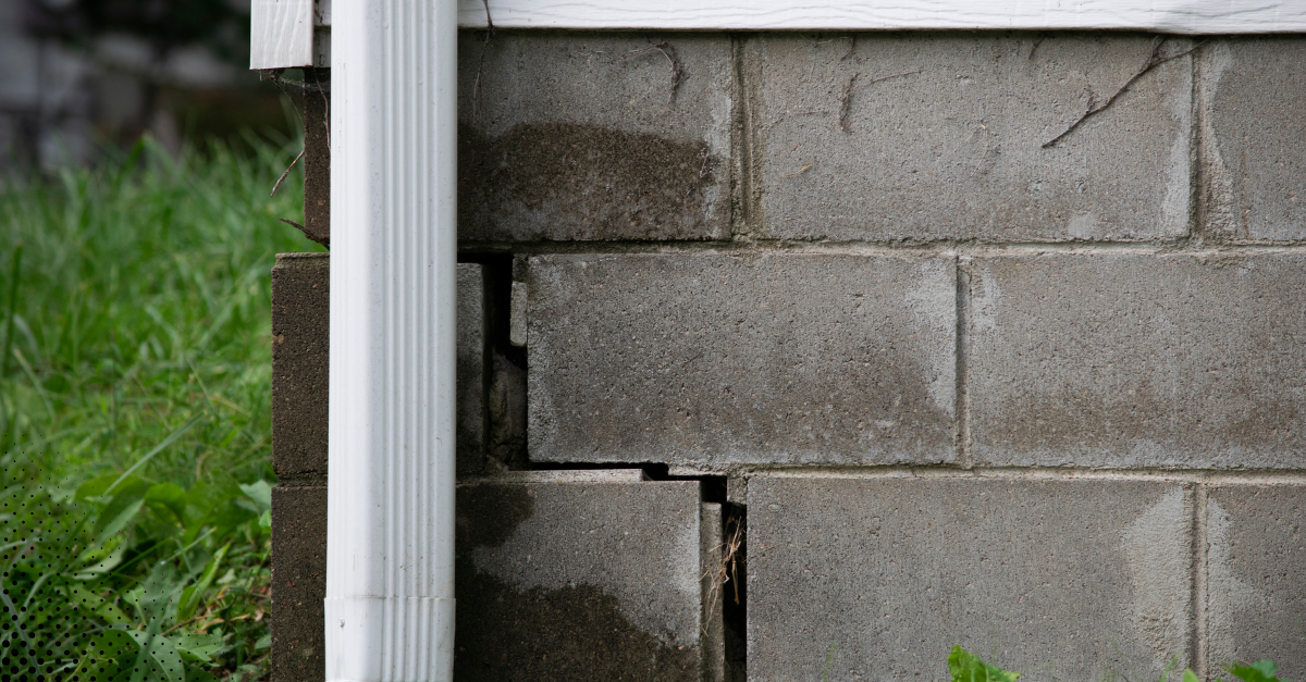Cracked cinder block foundation near the corner of a building.