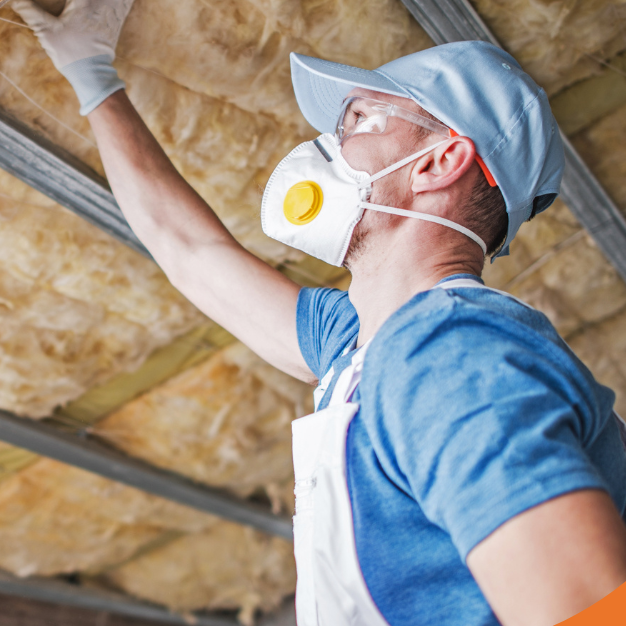 Inspector checking attic insulation while wearing safety gear.