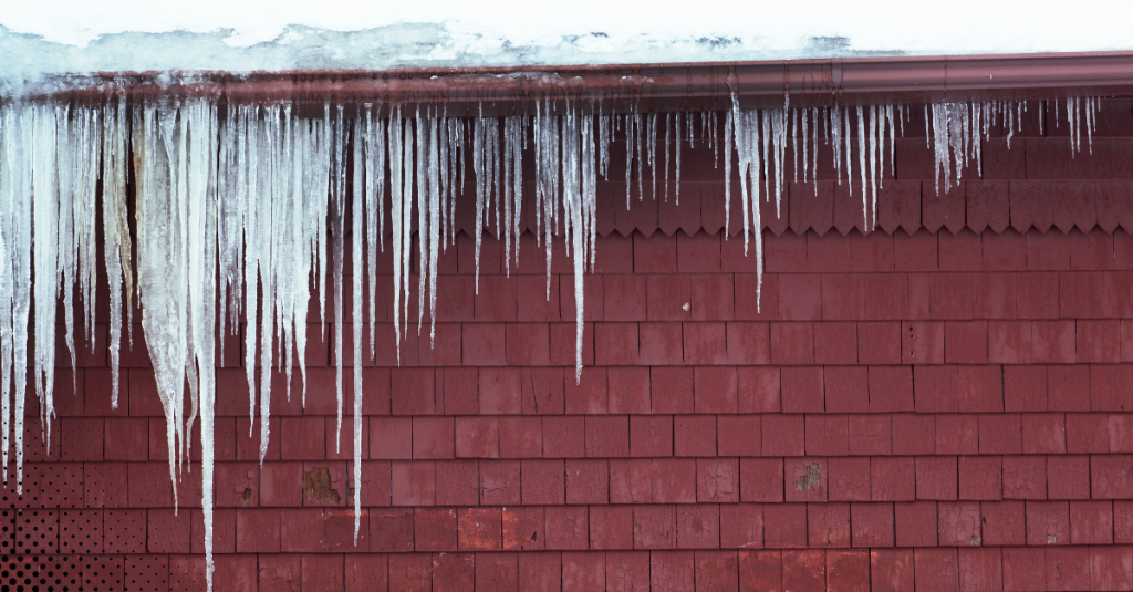 Long icicles hanging from the roof edge of a red wooden house.