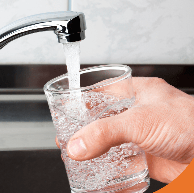 Hand filling a glass with clean drinking water from a kitchen faucet.